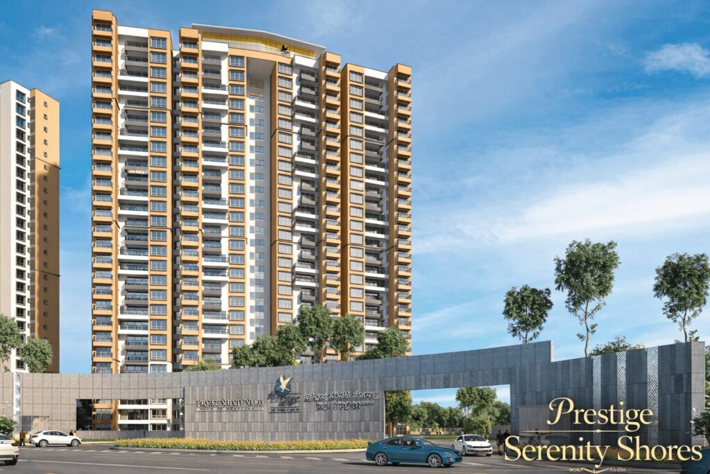 Prestige Serenity Shores grand entrance gate with modern stone façade, high-rise residential towers, landscaped frontage, and luxury apartments under a clear blue sky.